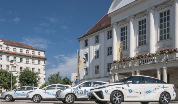Vier Wasserstoff-Autos stehen auf einem Platz. Dahinter befindet sich das Rathaus der Stadt Sonneberg.