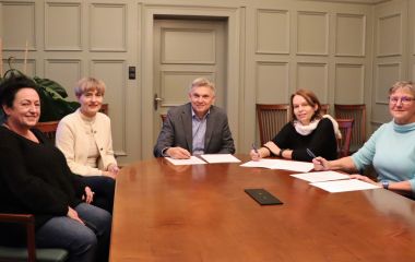 Vier Frauen und ein Mann sitzen an einem Tisch und unterzeichnen Verträge für eine Kooperation.