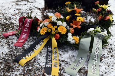Blumengebinde vor einem Denkmal auf dem Friedhof. Es liegt Schnee.
