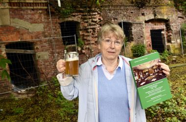 Eine Frau hält einen Krug mit Bier und ein grünes Buch in den Händen.