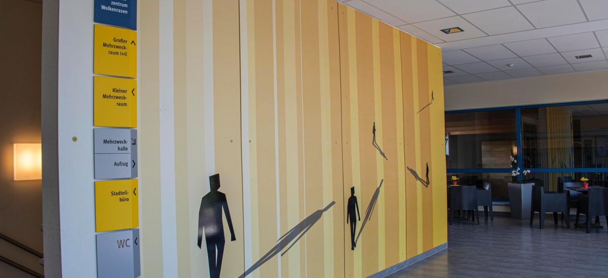 Auf einer gestreiften Wand sind Schatten von Menschen abgedruckt.