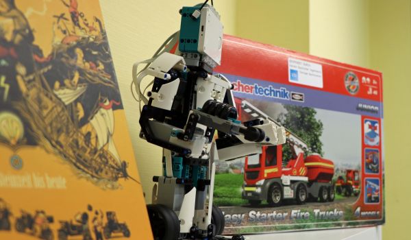 Auf einem Regal steht ein Roboter aus Bausteinen. Daneben ist eine Technikbaukausten mit einem Feuerwehrauto darauf.