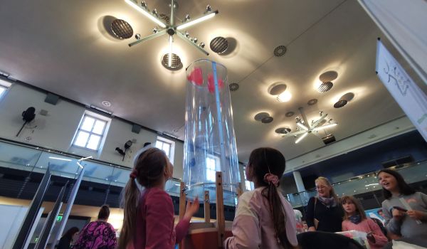 Kinder lassen Luftballons über eine Glasröhre aufsteigen.