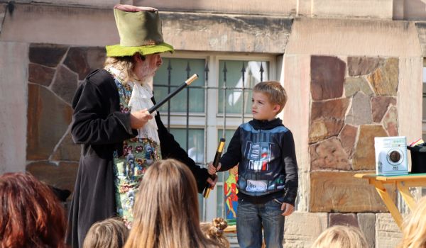 Ein Mann hält einen Zauberstab in der Hand. Er ist als Zauberer verkleidet. Rechts neben ihm steht ein kleiner Junge.