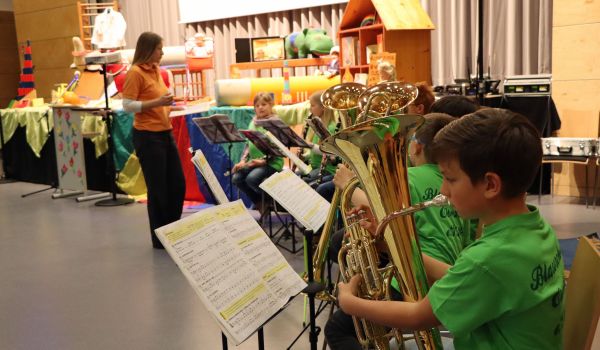 Kinder sitzen vor einer Bühne und spielen auf Blasinstrumenten.
