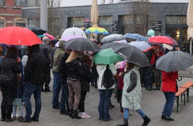 Eine Gruppe von Menschen sucht Schutz vor Schnee unter Regenschirmen. Sie befinden sich auf dem Piko-Platz.