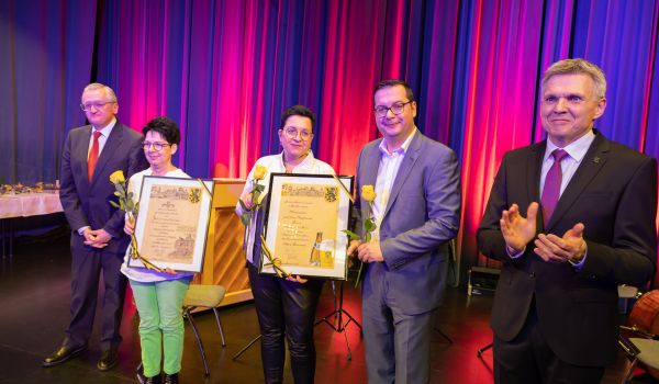 Auf einer Bühne stehen der Bürgermeister und Professor Dippold, welche ein Präsent an drei Personen überreichen.