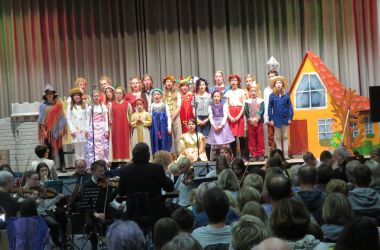Kinder in bunten Kostümen stehen auf einer Bühne und singen.