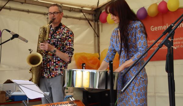Ein Mann mit Saxophone und eine Frau mit Trommel stehen auf einer Bühne. Im Hintergrund hängen Luftballons.