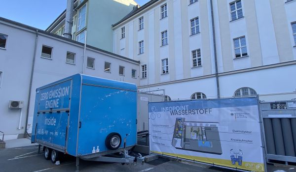 Ein blauer Anhänger steht neben einem Banner mit der Aufschrift: Infopoint Wasserstoff.