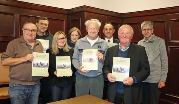 Mehrere Personen stehen in zwei Reihen. Sie halten ein Buch mit der Aufschrift: Höhnbach in den Händen.