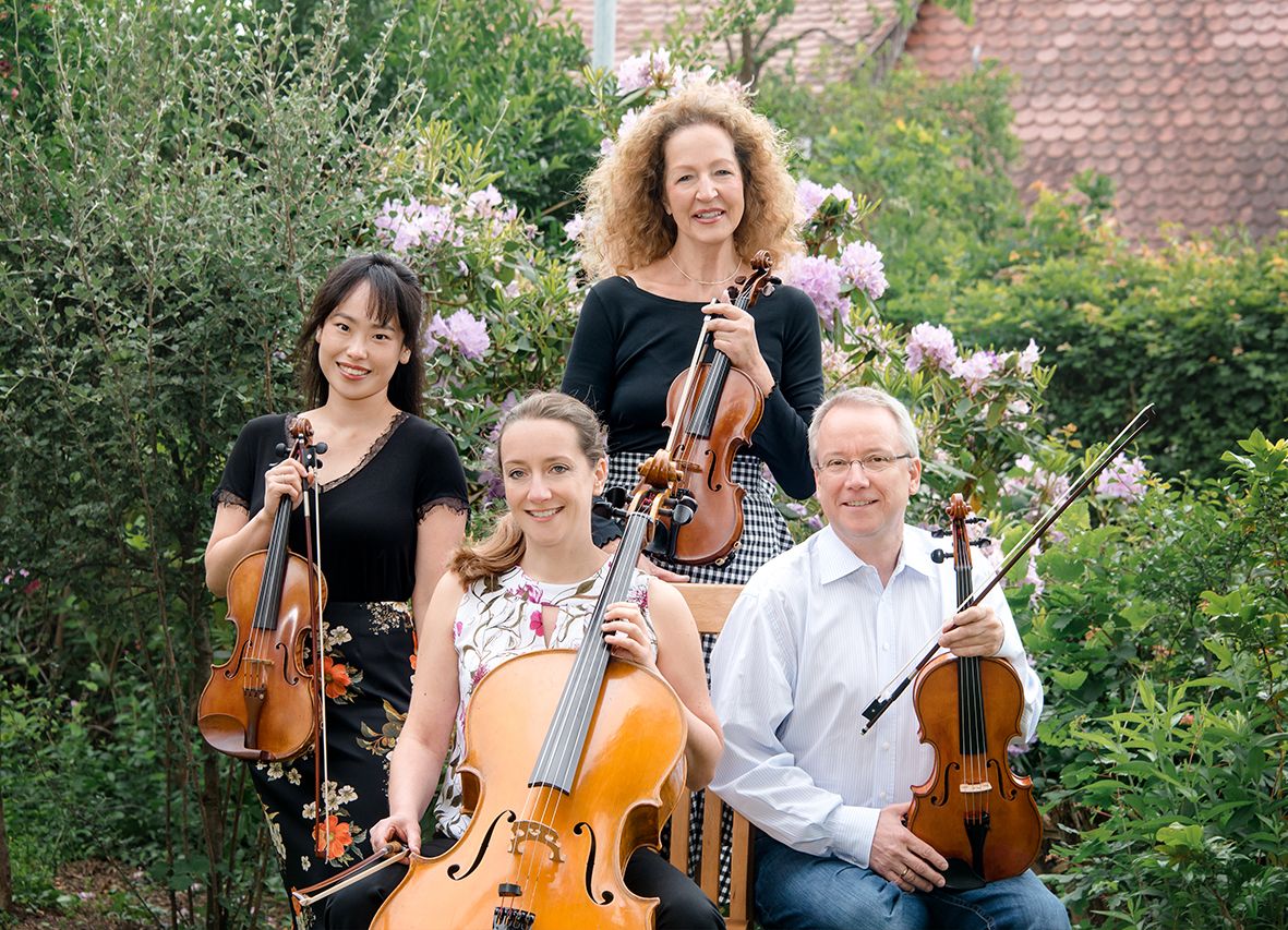 Vier Musiker mit Violinen, Violas und Cellos sitzen in einem Garten.