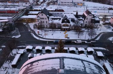 Drohnenaufnahme mit Blick auf den Bahnhof und das Rathaus. Vor dem Rathaus ist Weihnachtsmarkt. Es liegt Schnee.
