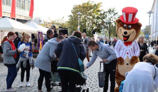 Eine Person im Bärenkostüm mit Zylinder läuft durch die Stadt. Viele Menschen stehen außen herum.