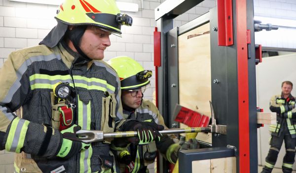 Zwei Feuerwehrmänner hebeln eine Übungstür auf.