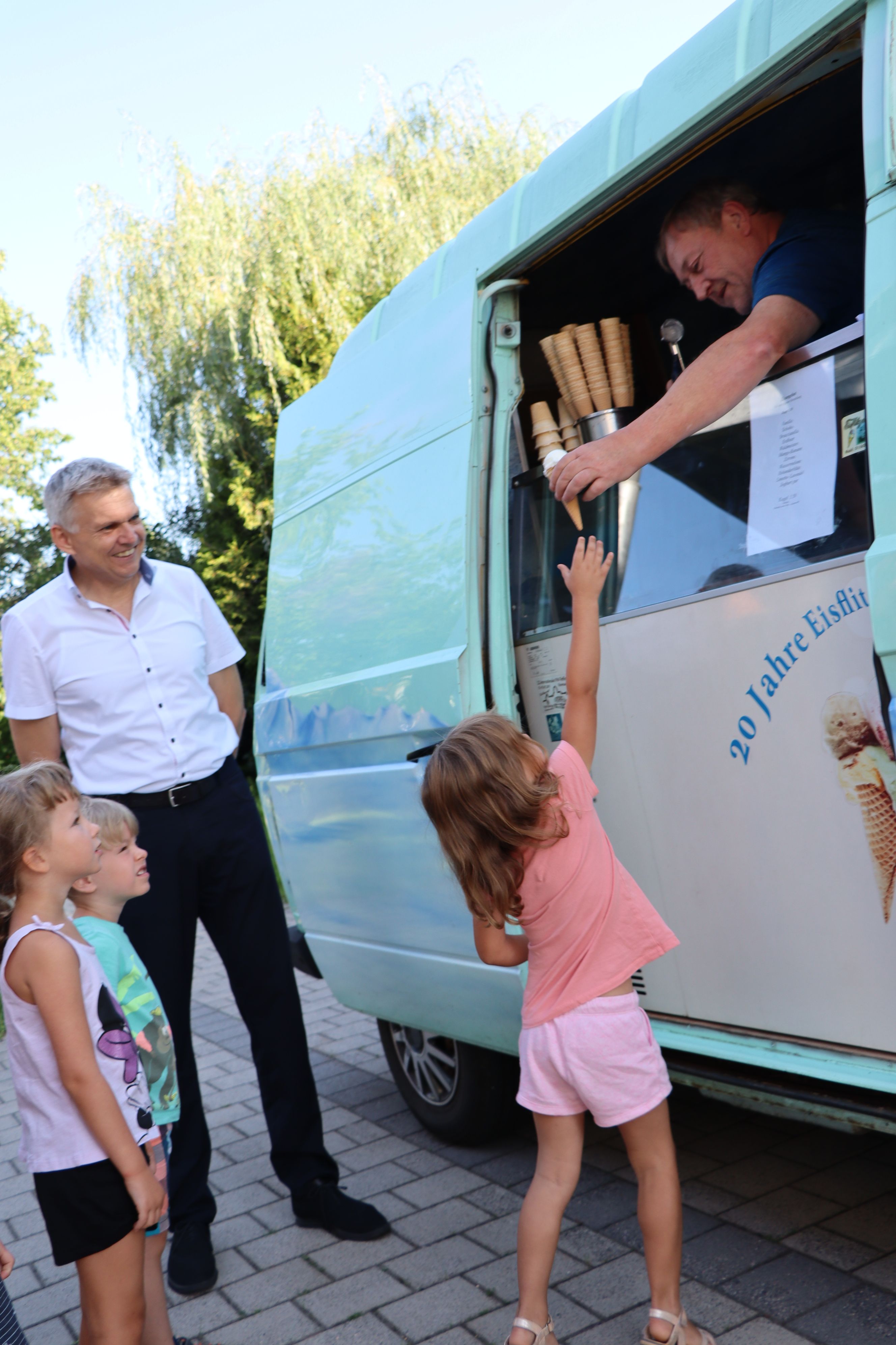 Ein Mann reicht einem Kind ein Eis aus einem Auto. Daneben steht der Bürgermeister der Stadt Sonneberg.