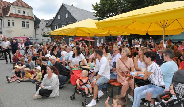 Viele Menschen sitzen auf Bänken unter Sonnenschirmen.