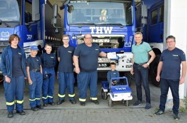 Mitglieder des Technischen Hilfswerks Sonneberg stehen mit dem Bürgermeister der Stadt Sonnebrg in einer Reihe. Im Hindergrund sind blaue THW-Einsatzfahrzeuge.