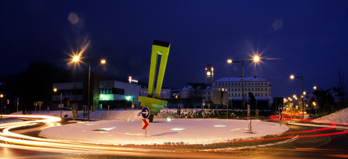 Ein Kreisverkehr bei Nacht. Darauf steht ein beleuchteter Kreisel aus Stahl. Im Hintergrund sieht man das Rathaus der Stadt Sonneberg.