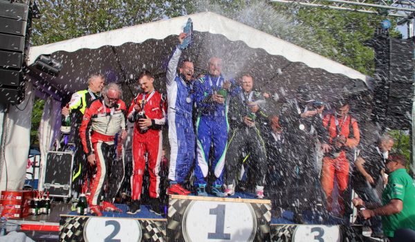 Männer in Rennfahreranzügen stehen auf einem Podest und feiern.