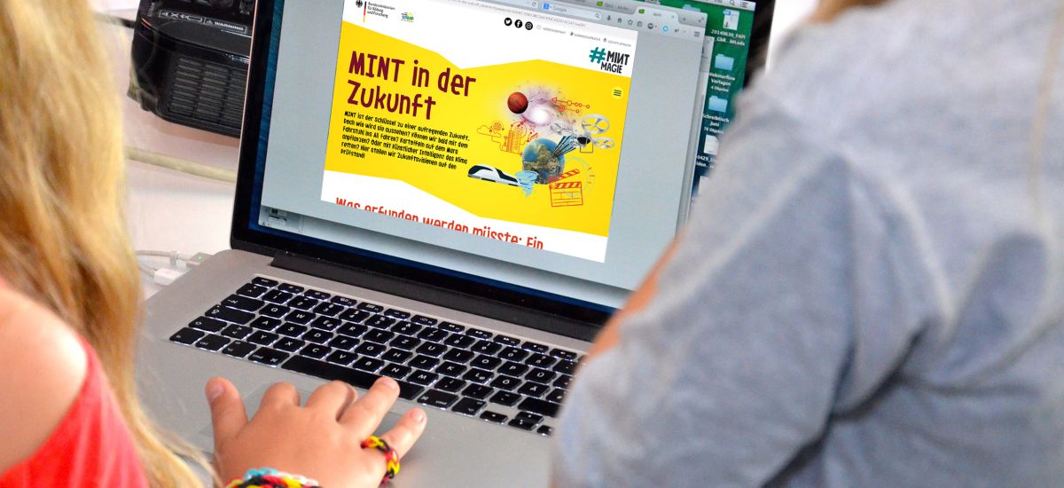 Kinder sitzen vor einem Laptop. Auf dem Laptop steht MINT in der Zukunft.
