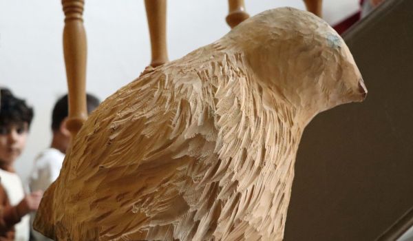 Ein aus Holz geschnitzter Vogel sitzt auf einem Sockel.