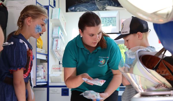 Eine Frau vom Jugendrotkreuz zeigt Kindern die Ausstattung eines Krankenwagens.