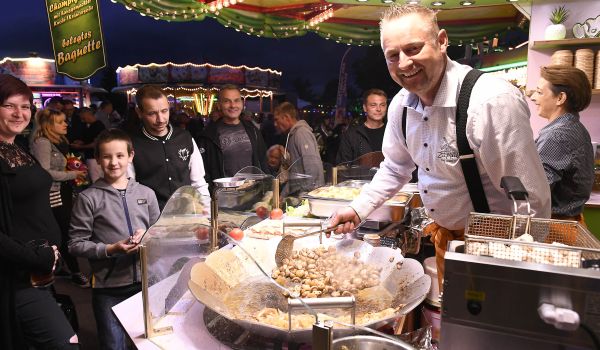 Ein Mann steht in einem Verkaufsstand mit Essen. Davor stehen Kunden.