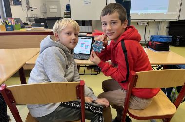 Zwei Kinder sitzen in einem Klassenzimmer an einem Laptop.