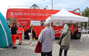 Auf dem Rathausplatz steht ein roter offnener Doppelstockbus. Er trägt die Aufschrift: Herzsache Lebenszeit, Info-Tag.