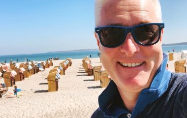 Ein Mann mit Sonnenbrille macht ein Selfie am Strand.