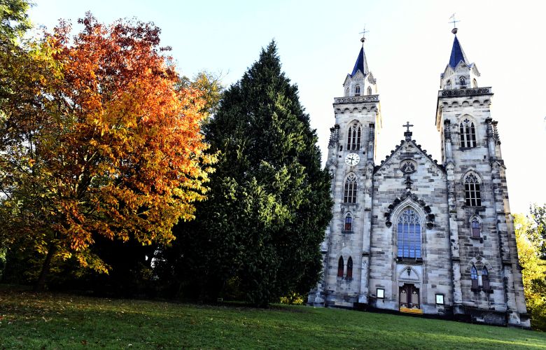 Eine Kirche mit zwei Türmen auf einem grünen Hügel mit Bäumen.