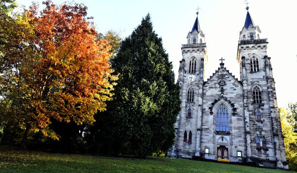 Eine Kirche mit zwei Türmen auf einem grünen Hügel mit Bäumen.