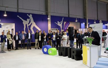 Ein Mann steht hinter einem Mikrofon. Außenrum stehen Menschen.