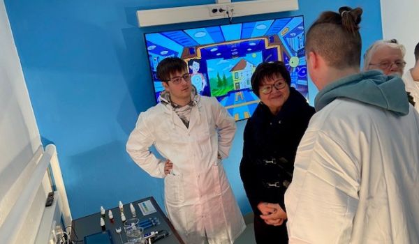 Zwei Jugendliche in weißen Kitteln erklären Experimente für Interessierte.