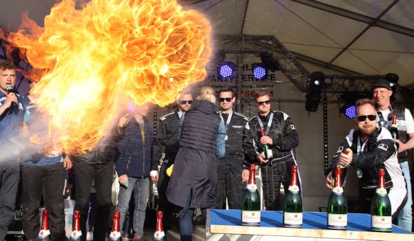 Die Gewinner stehen auf einer Bühne. Vor ihnen ist eine Stichflamme.