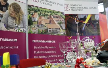 An einem Messestand stehen verschiedene Glasobjekte.