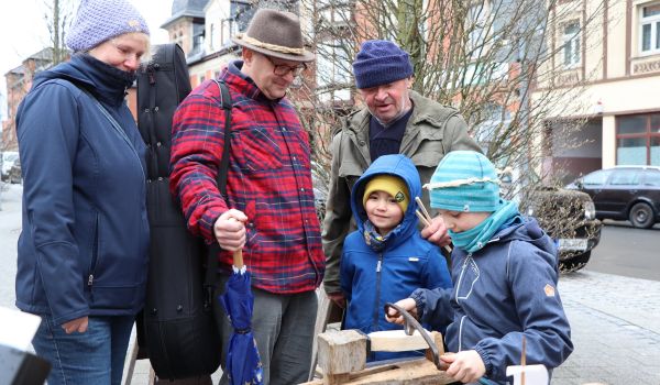 Ein Mann zeigt Kindern wie sie ein Boot aus Holz schnitzen.
