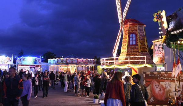 Beleuchtete Fahrgeschäfte und Verkaufsstände bei Nacht.