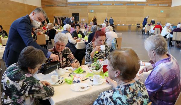 Frauen sitzen an einem Tisch. Ein Mann schenkt Kaffee ein.
