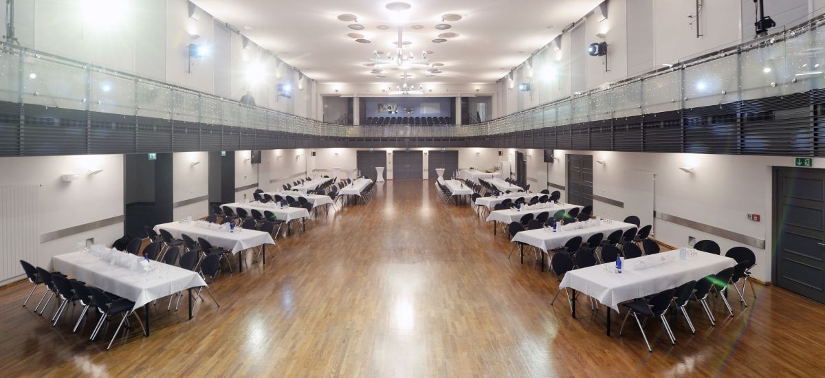 In einem modernen Saal stehen Tische mit Stühlen daran.