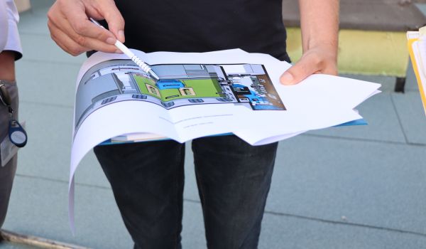 Eine Person hält einen Bauplan un einen Stift in den Händen.