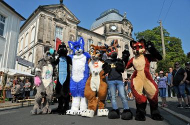 Sechs Personen in Tierkostümen aus Plüsch stehen vor einem alten Sandstein-Gebäude. Es ist das Spielzeugmuseum der Stadt Sonneberg.