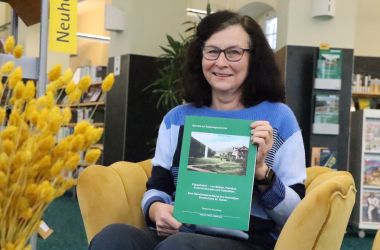 Eine Frau sitzt auf einem Sessel und hält eine A4-große Publikation in die Kamera.