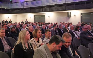 Menschen sitzen in Stuhlreihen nebeneinander.