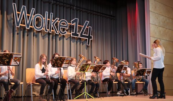 Kinder sitzen auf einer Bühne und spielen auf Blasinstrumenten.