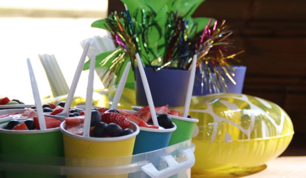 Bunte Becher mit Obst darin. Im Hintergrund stehen Becher mit farbenfrohen Partypickern.