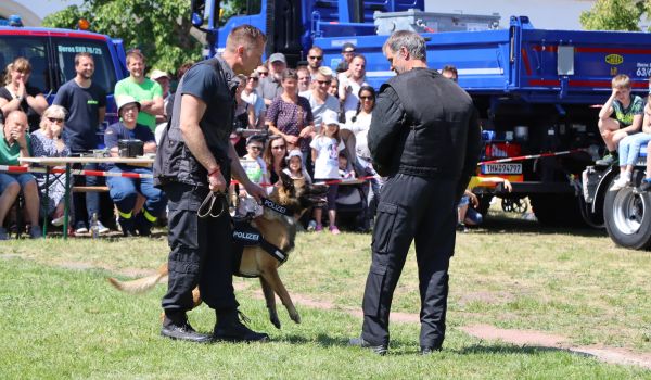 Ein Mann im Schutzanzug steht neben einem Mann mit Spürhund.