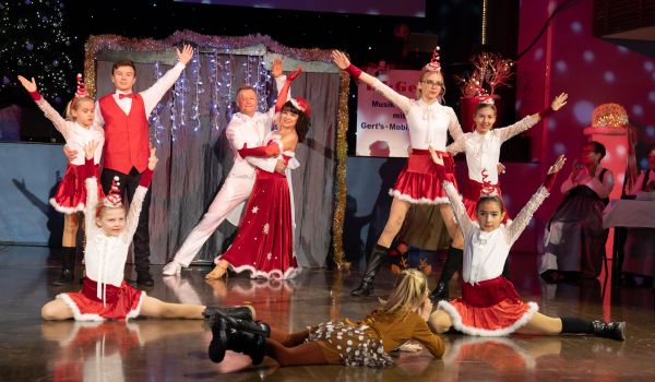 KInder und Erwachsene in weihnachtlicher Kleidung tanzen auf einer Bühne.