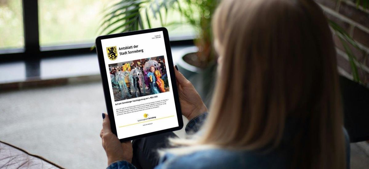 Eine Frau sitzt mit einem Tablet auf der Couch.